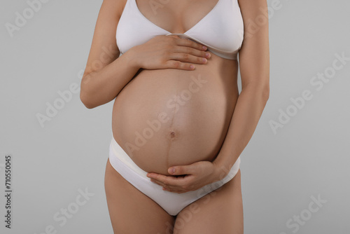Pregnant woman in stylish comfortable underwear on grey background, closeup