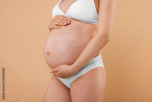 Pregnant woman in stylish comfortable underwear on beige background, closeup