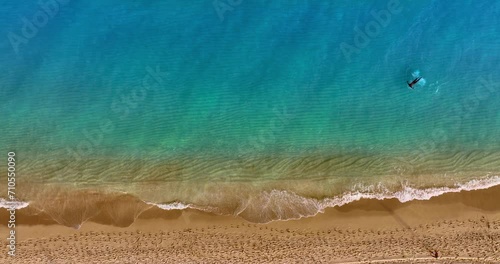 One person swimming in the azure water near the sandy beach. Waves splash by the shore. Top view. photo