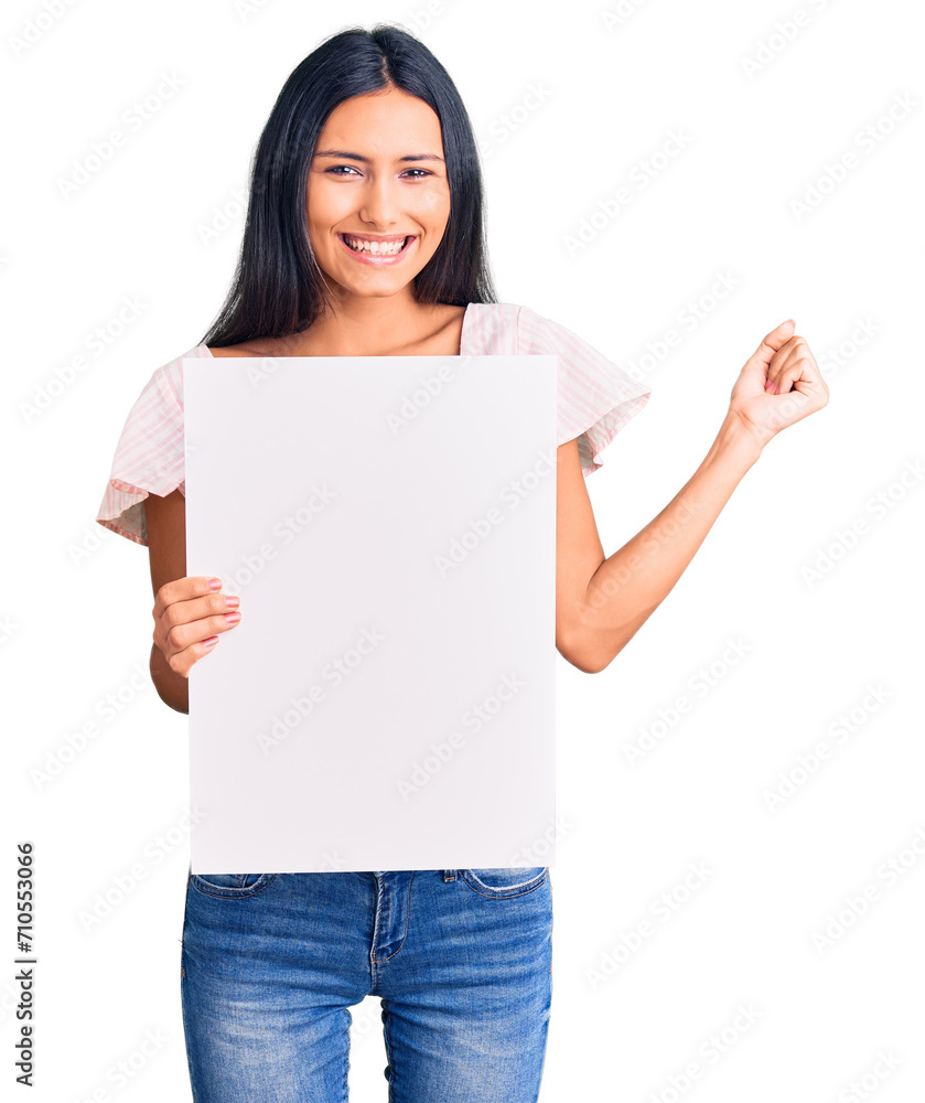 Young beautiful latin girl holding blank empty banner screaming proud, celebrating victory and success very excited with raised arms Young beautiful latin girl holding blank empty banner screaming proud, celebrating victory and success very excited with raised arms