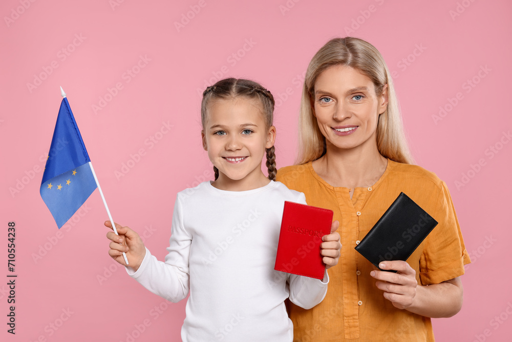 Immigration. Happy woman with her daughter holding passports and flag of European Union on pink background Immigration. Happy woman with her daughter holding passports and flag of European Union on pink background