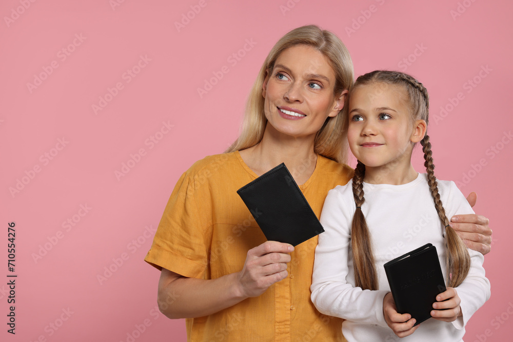 Immigration. Happy woman and her daughter with passports on pink background, space for text Immigration. Happy woman and her daughter with passports on pink background, space for text