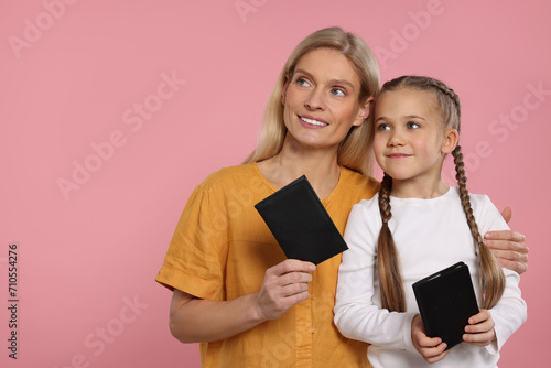 Immigration. Happy woman and her daughter with passports on pink background, space for text photo