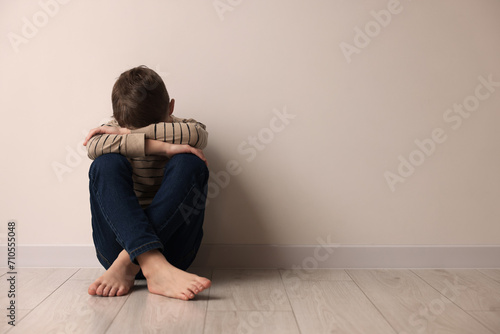 Child abuse. Upset boy sitting on floor near beige wall indoors, space for text