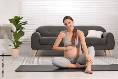 Pregnant woman sitting on yoga mat at home, space for text