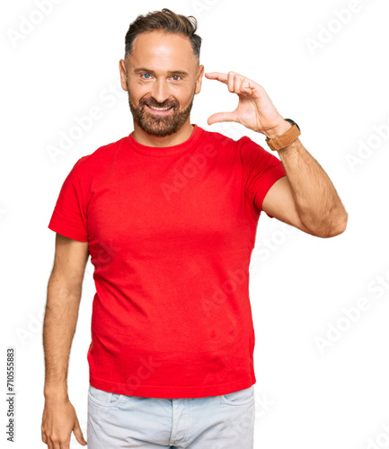 Handsome middle age man wearing casual red tshirt smiling and confident gesturing with hand doing small size sign with fingers looking and the camera. measure concept.