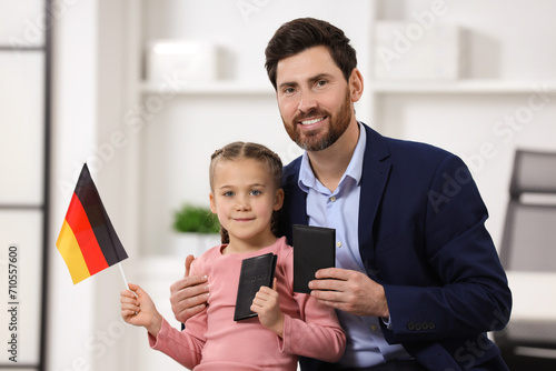 Immigration. Happy man with his daughter holding passports and flag of Germany indoors photo