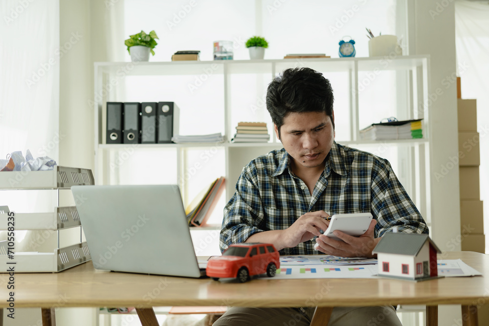 Young Asian man calculates car payments Home installments in financial planning and income Asset approval concepts, buying cars and houses, checklist, home loans, home taxes Young Asian man calculates car payments Home installments in financial planning and income Asset approval concepts, buying cars and houses, checklist, home loans, home taxes