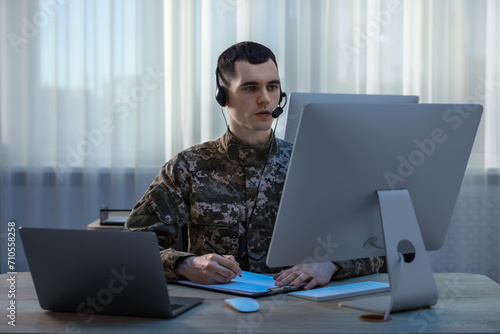 Military service. Young soldier in headphones working at wooden table in office