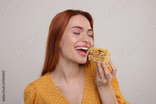 Young woman eating piece of tasty cake on light grey background