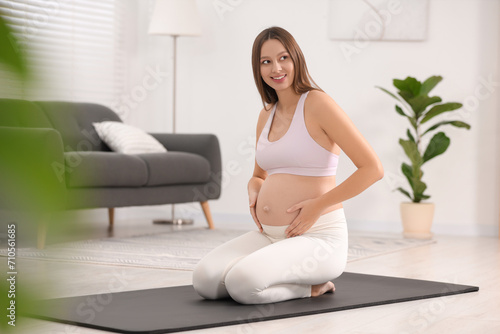 Pregnant woman sitting on yoga mat at home