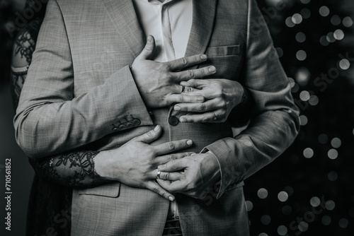 monochrome close-up of a couple's hands clasped around a man in a suit, with the woman's hand wearing a wedding ring.
