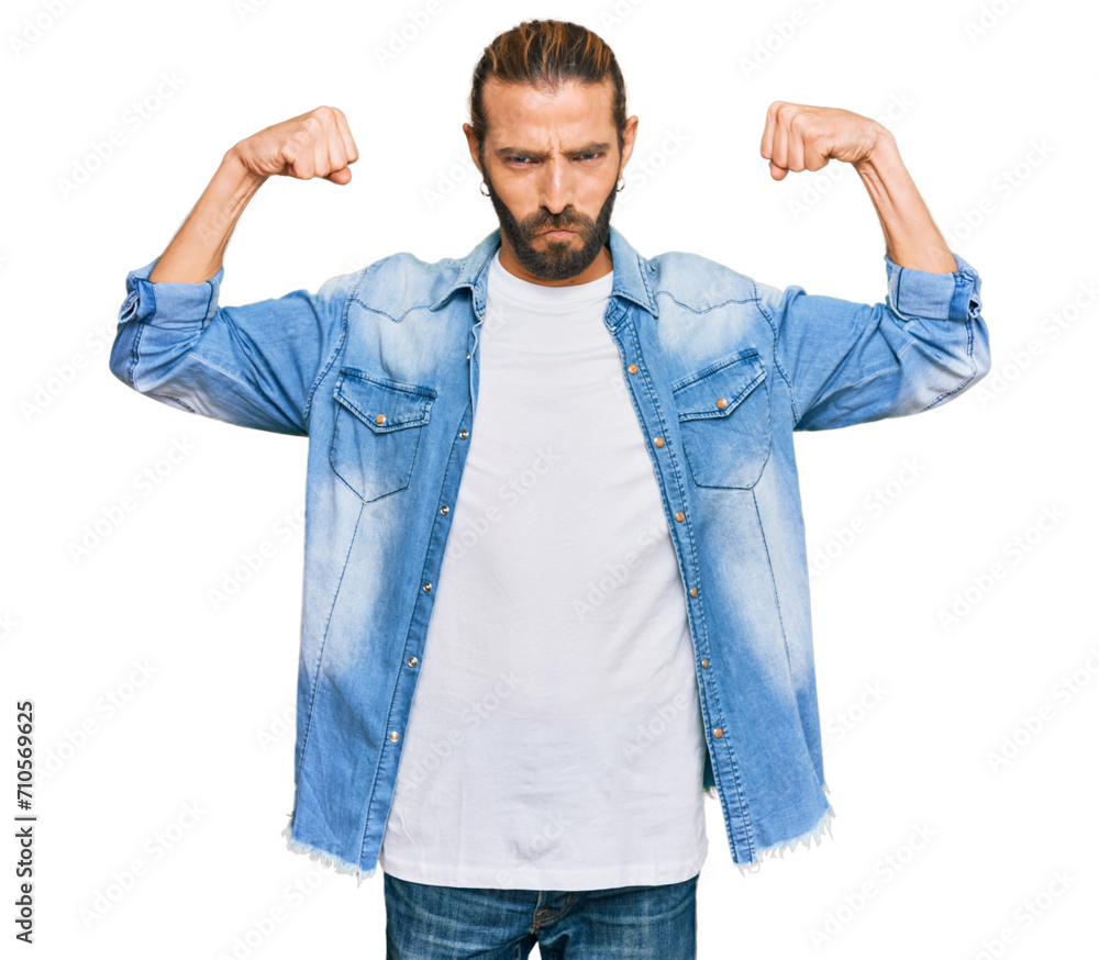 Attractive man with long hair and beard wearing casual denim jacket showing arms muscles smiling proud. fitness concept. Attractive man with long hair and beard wearing casual denim jacket showing arms muscles smiling proud. fitness concept.