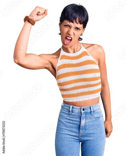 Young brunette woman with short hair wearing casual clothes angry and mad raising fist frustrated and furious while shouting with anger. rage and aggressive concept.