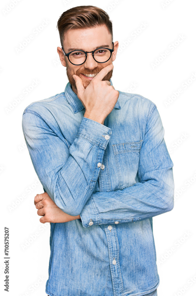 Young redhead man wearing casual denim shirt looking confident at the camera smiling with crossed arms and hand raised on chin. thinking positive. Young redhead man wearing casual denim shirt looking confident at the camera smiling with crossed arms and hand raised on chin. thinking positive.