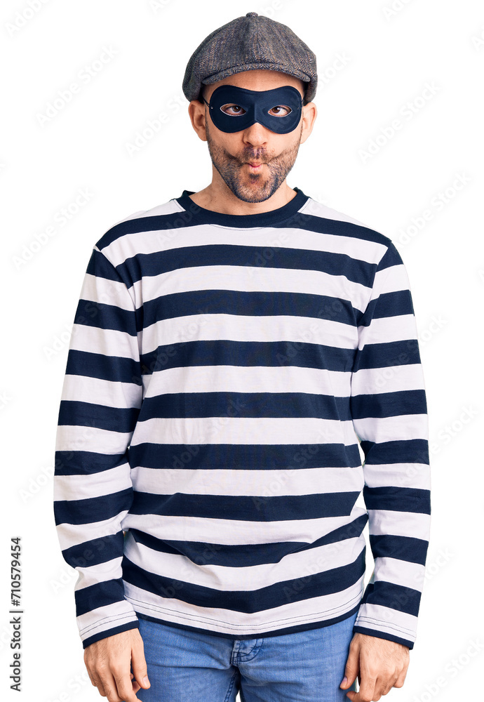 Young handsome man wearing burglar mask making fish face with lips, crazy and comical gesture. funny expression. Young handsome man wearing burglar mask making fish face with lips, crazy and comical gesture. funny expression.