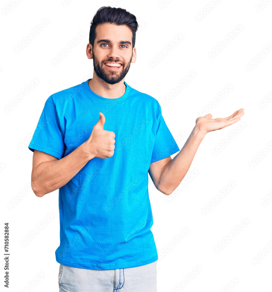 Young handsome man with beard wearing casual t-shirt showing palm hand and doing ok gesture with thumbs up, smiling happy and cheerful Young handsome man with beard wearing casual t-shirt showing palm hand and doing ok gesture with thumbs up, smiling happy and cheerful