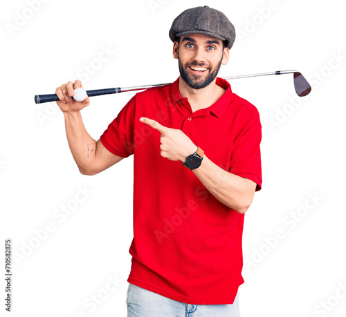 Young handsome man with beard playing golf holding club and ball smiling happy pointing with hand and finger