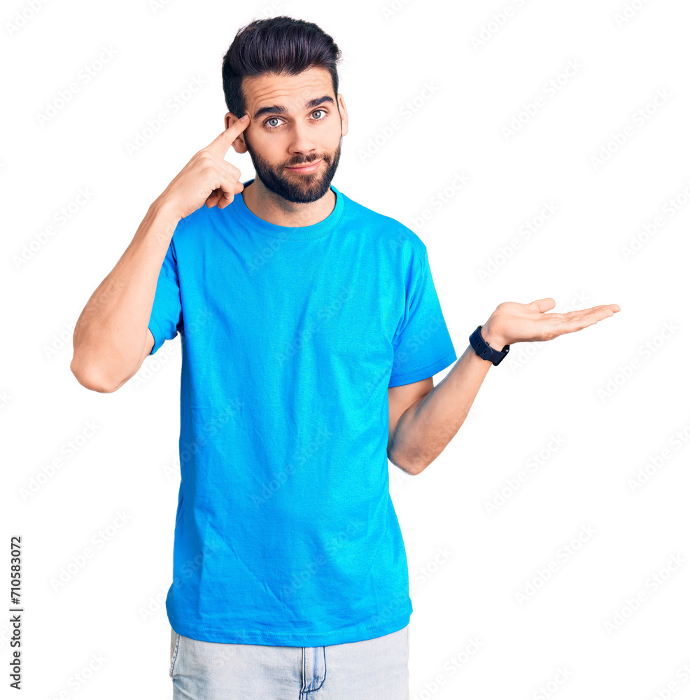Young handsome man with beard wearing casual t-shirt confused and annoyed with open palm showing copy space and pointing finger to forehead. think about it. Young handsome man with beard wearing casual t-shirt confused and annoyed with open palm showing copy space and pointing finger to forehead. think about it.