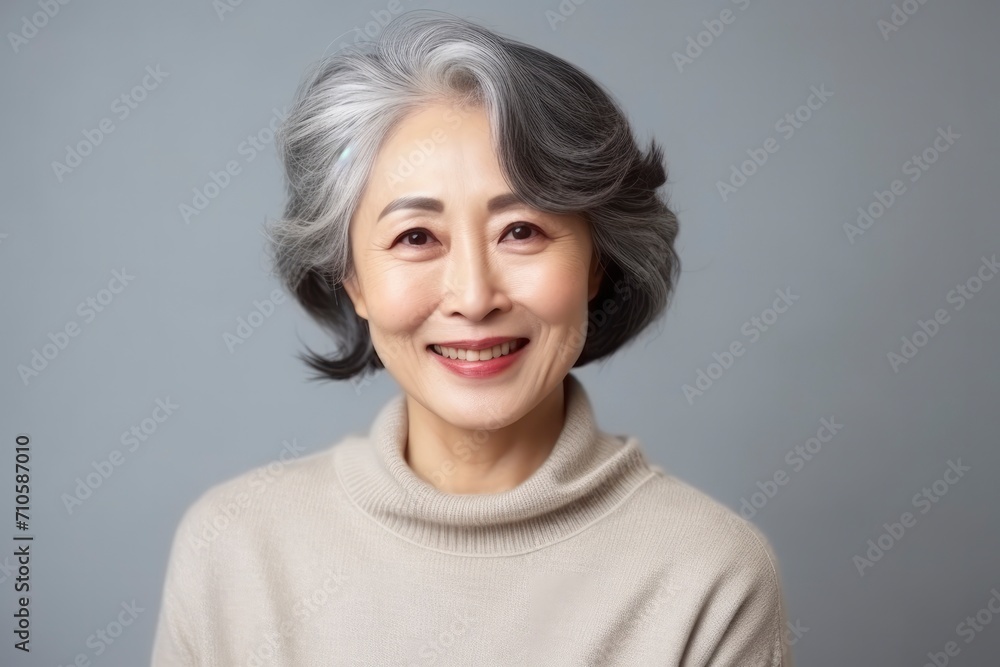 Portrait of beautiful middle-aged Asian woman on gray background. Gorgeous Korean woman 50-60 years old smiles, looks at camera. Concept of happy pensioner, old age, cosmetology and face lifting Portrait of beautiful middle-aged Asian woman on gray background. Gorgeous Korean woman 50-60 years old smiles, looks at camera. Concept of happy pensioner, old age, cosmetology and face lifting