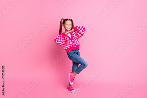 Full size photo of cute positive schoolgirl with tails dressed knit cardigan jeans hold hands under chin isolated on pink color background