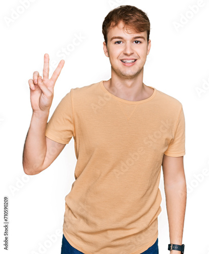 Young caucasian man wearing casual clothes smiling looking to the camera showing fingers doing victory sign. number two.