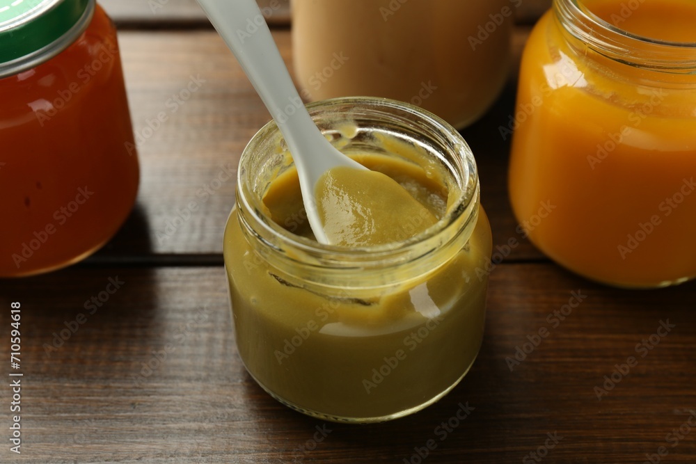 Tasty baby food in jar and spoon on wooden table, closeup Tasty baby food in jar and spoon on wooden table, closeup