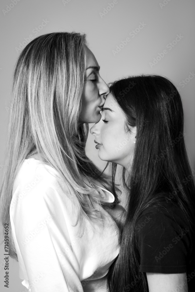 tender black and white portrait of a mother with closed eyes kissing her teenage daughter on the forehead