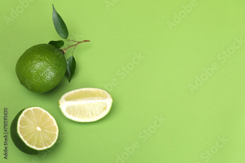 Flat lay composition with fresh limes and leaves on green background. Space for text