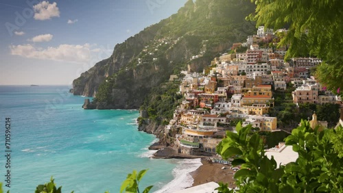 Camera moves between green leaves, overlooking the beach with turquoise water, colorful houses and mountains in Positano village. Beautiful Positano village, Amalfi coast, Italy. Steadycam shot, 4K photo