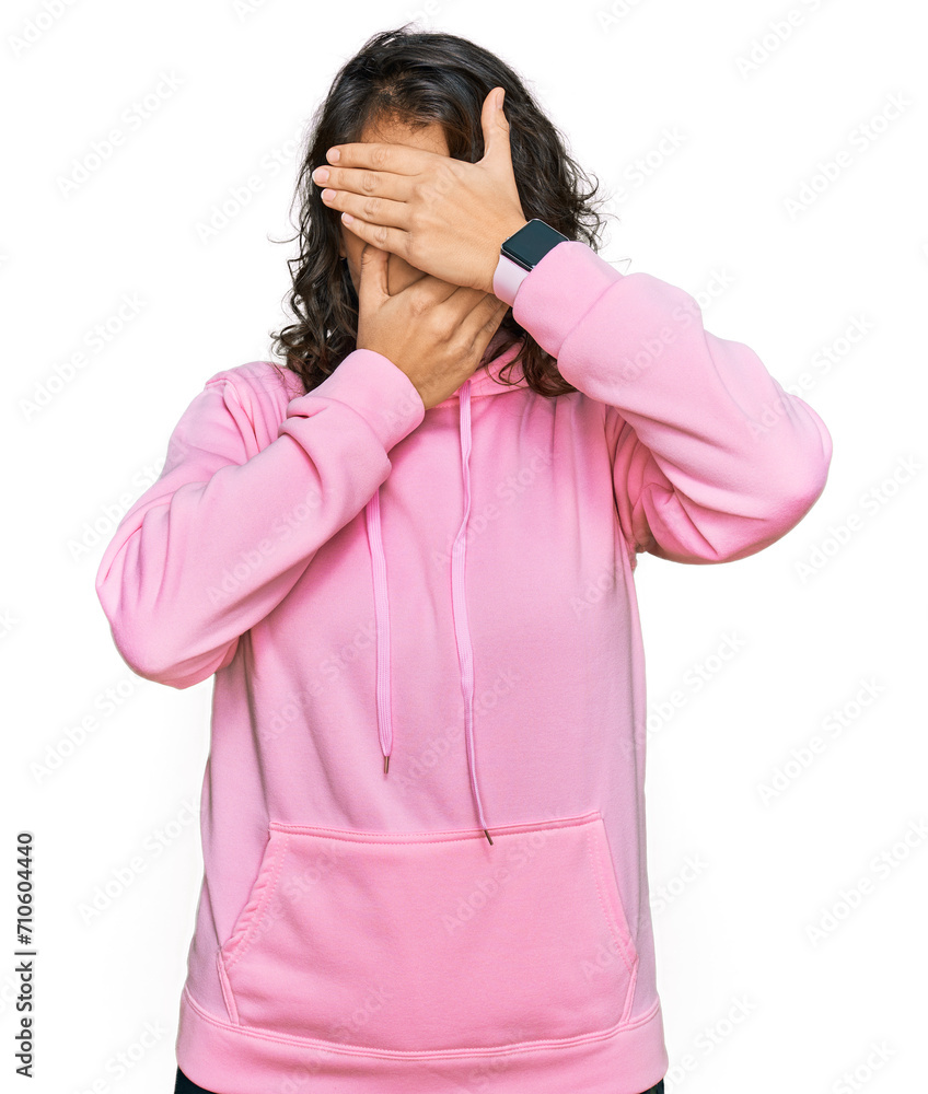 Young hispanic woman wearing casual sweatshirt covering eyes and mouth with hands, surprised and shocked. hiding emotion Young hispanic woman wearing casual sweatshirt covering eyes and mouth with hands, surprised and shocked. hiding emotion