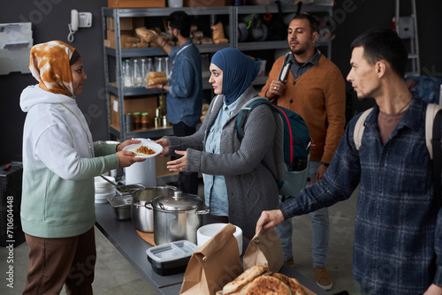 High angle view at group of Middle Eastern people receiving hot meals at soup kitchen or refugee support center with volunteer helping