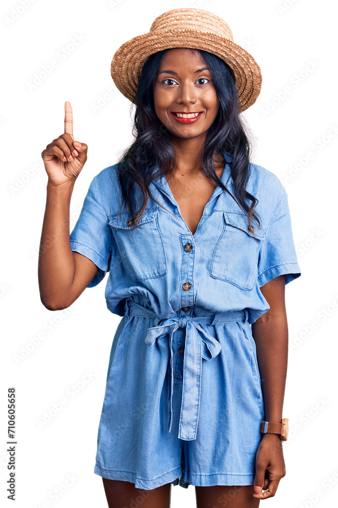 Young indian girl wearing summer hat showing and pointing up with finger number one while smiling confident and happy. Young indian girl wearing summer hat showing and pointing up with finger number one while smiling confident and happy.