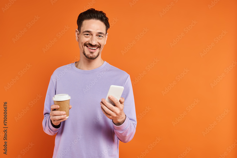 smiling man in glasses holding coffee to go and using smartphone on orange background, caffeine smiling man in glasses holding coffee to go and using smartphone on orange background, caffeine