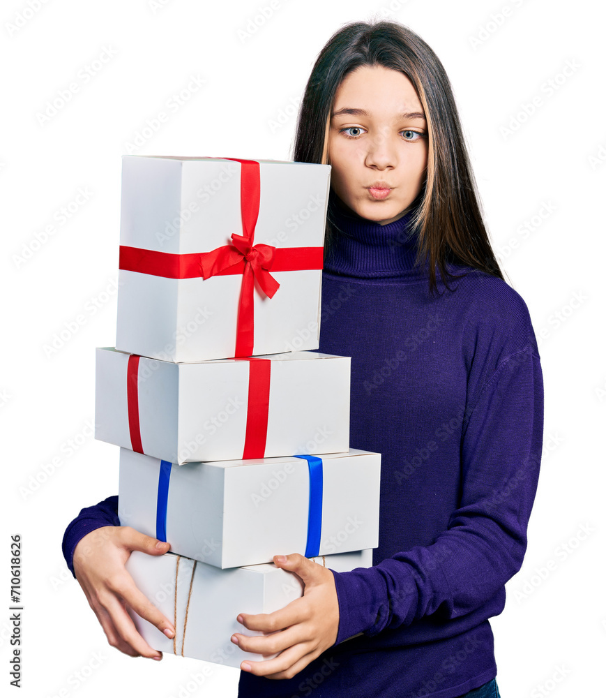 Young brunette girl with long hair holding gifts making fish face with mouth and squinting eyes, crazy and comical.