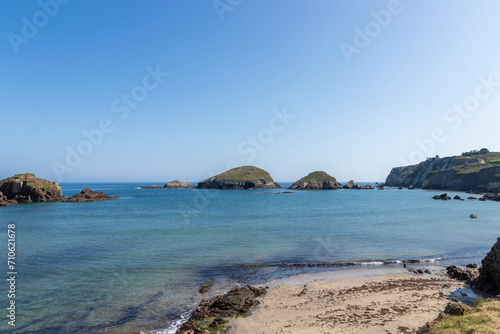 a tranquil beach with clear blue waters, scattered rocky islands, under a bright sky, creating a picturesque landscape