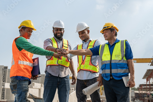 Group of diverse teamwork civil engineers foreman and workers wear safety vests with helmets stand and join hands together ready to work at construction site factory produce precast concrete