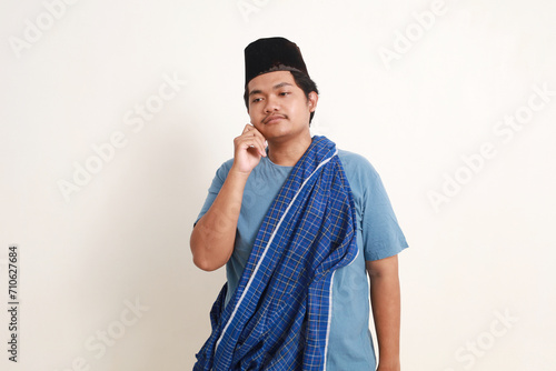 Confused young asian muslim boy standing while thinking or dreaming something. Isolated on white photo