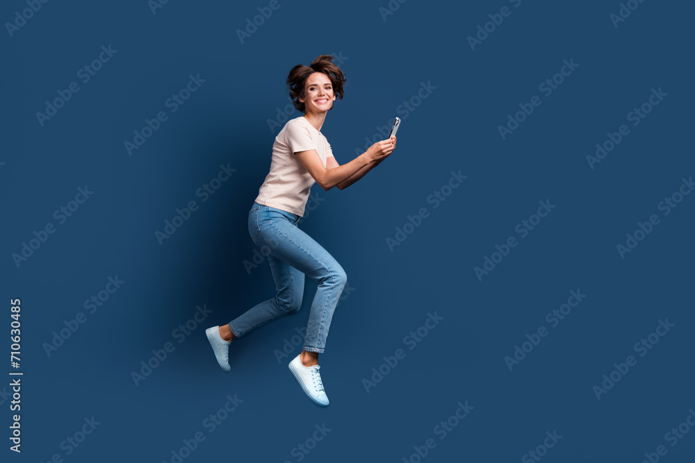 Full length photo of lovely young lady running hold telephone hurry shopping dressed white garment isolated on dark blue color background