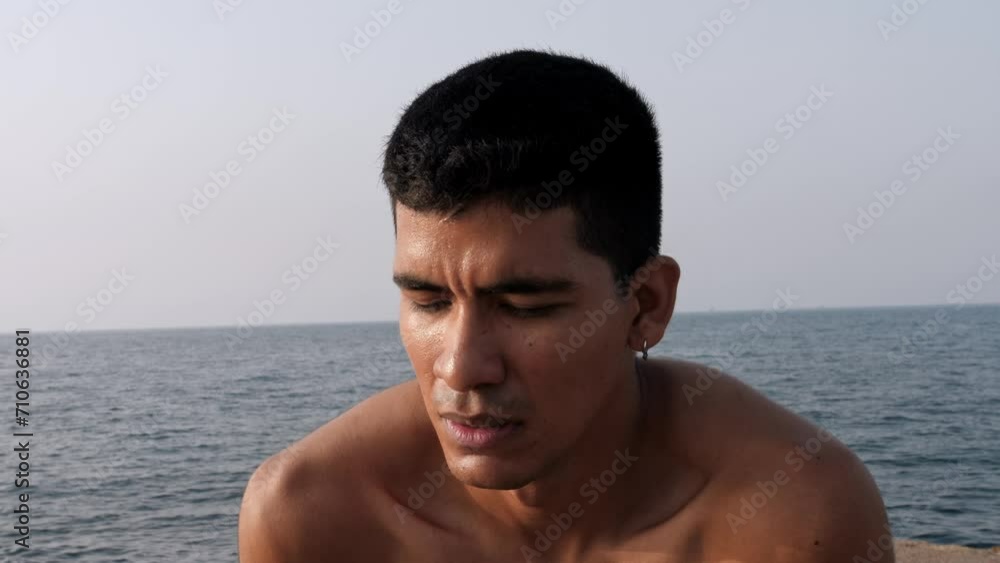 Young latino man ends running by the sea and rests with his arms on his legs Young latino man ends running by the sea and rests with his arms on his legs