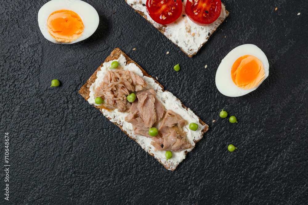 Ingredients for sandwich with boiled egg, cherry tomatoes, canned tuna, garlic and spices over black grunge background. High quality photo