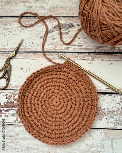 Unfinished crochet round shape placemat on a wooden surface