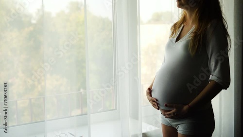 A pregnant woman strokes her belly with her hand. The girl's stomach itches. The child pushes in the stomach. Caring for the newborn. The wife is waiting for her husband near the window. photo
