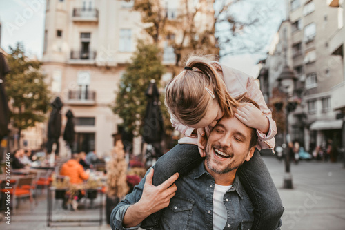 Father enjoying time with daughter on shoulders in city square photo