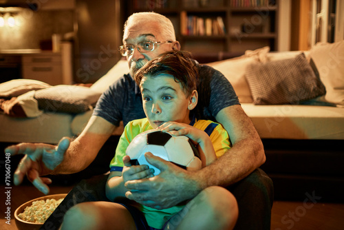 Grandfather watching a football game with his grandson at home photo