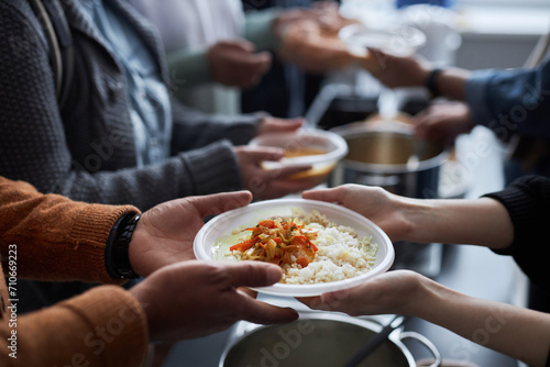 Close up of hands holding plastic plate with rice, unrecognizable volunteer helping refugees at soup kitchen