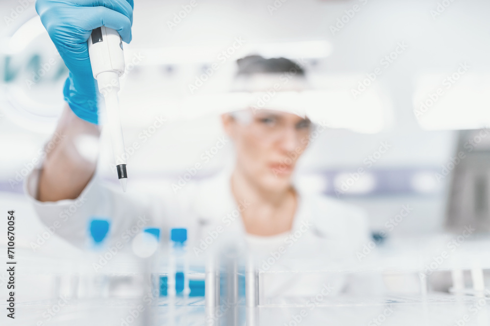 Fototapeta premium Blurred unrecognizable woman scientist working conducts research in modern bio laboratory. Female doctor laboratory assistant do tests, taking samples from test tubes with pipette