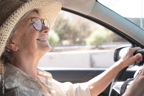 Smiling senior woman driving a car looking back in the rearview mirror