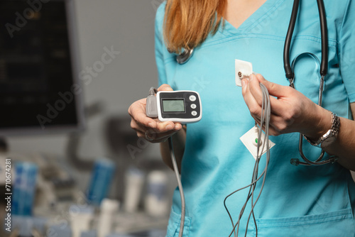 Doctor showing ECG holter monitor to patient in pediatric clinic. Holter monitoring device in a doctor hands before a diagnostic. Preparation for a heart rhythm diagnistic. Professional medicine.