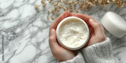 Moisturizing hand cream in jar on marble background with cosy sweater photo